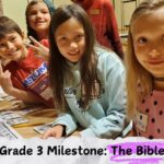 Children smile at the camera while working on a Grade 3 Milestone project titled "The Bible" with a person assisting.
