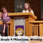 Three people stand at a church lectern during a Grade 4 worship milestone. Religious banners and candles are visible in the background.