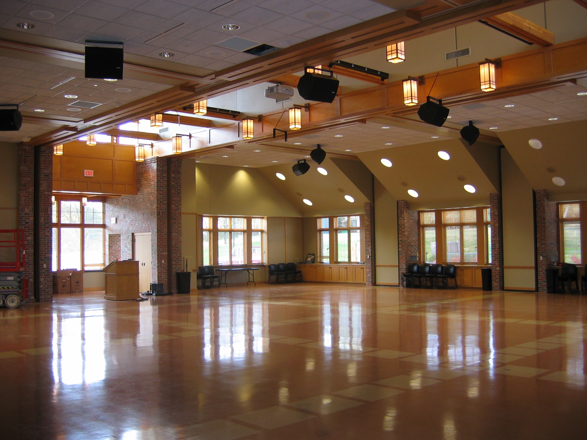 Spacious, well-lit interior with wooden beams and large windows. Empty chairs and equipment are visible. Venue appears ready for events or gatherings.