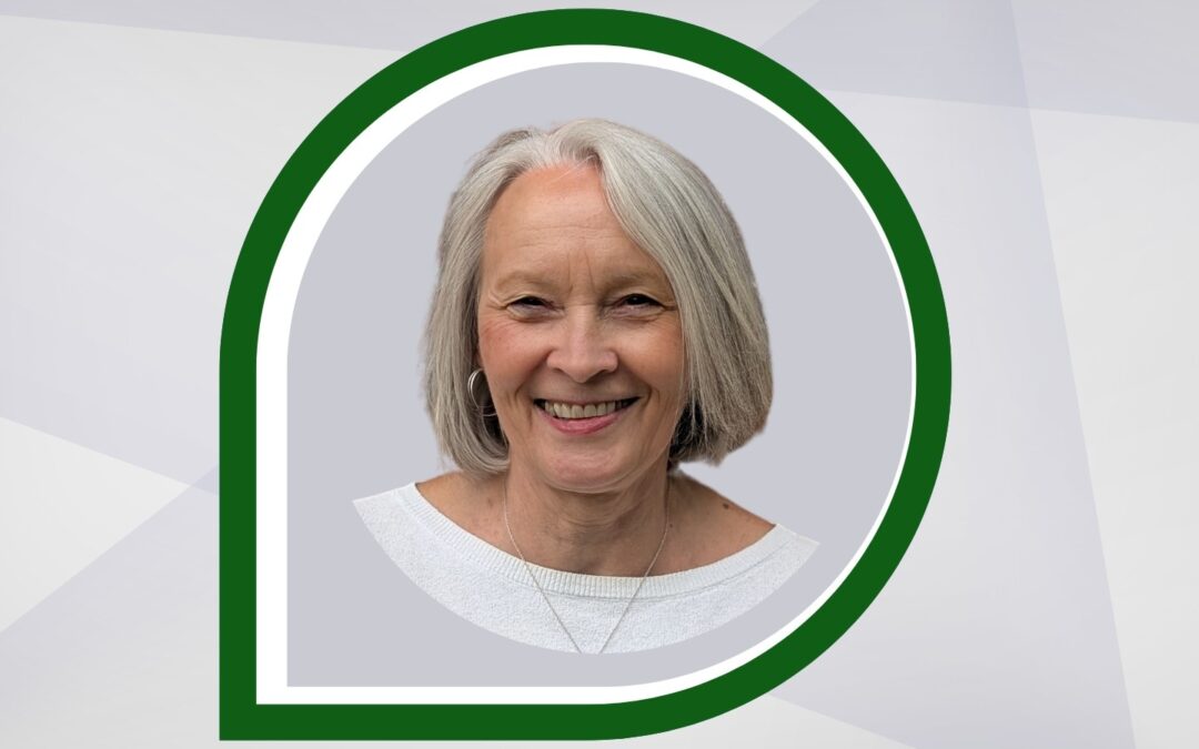 A person with short gray hair smiles in a portrait framed by a green and white speech bubble design, against a geometric gray background.