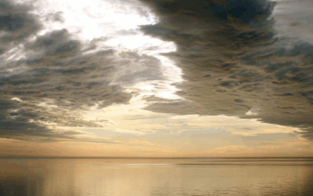 Dramatic sky over calm sea, golden hour hues reflecting on water. Thick, textured clouds create a striking contrast with serene horizon. No landmarks visible.